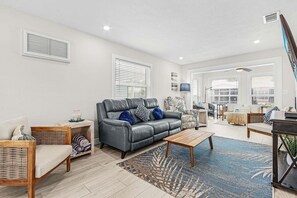 A modern living room with a grey sofa, wooden side table, wicker chair, and a blue patterned rug.