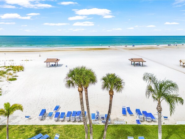 A beach with white sand, blue lounge chairs, and palm trees.