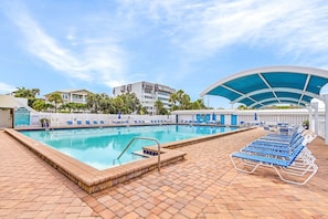 Uma piscina com espreguiçadeiras e área coberta, cercada por edifícios e palmeiras.