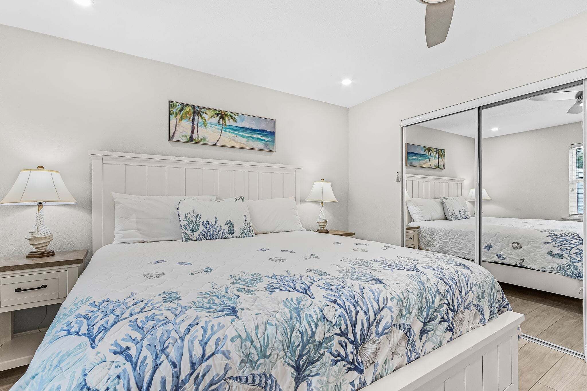 A bedroom with a bed, nightstands, lamps, a painting, and a mirror.