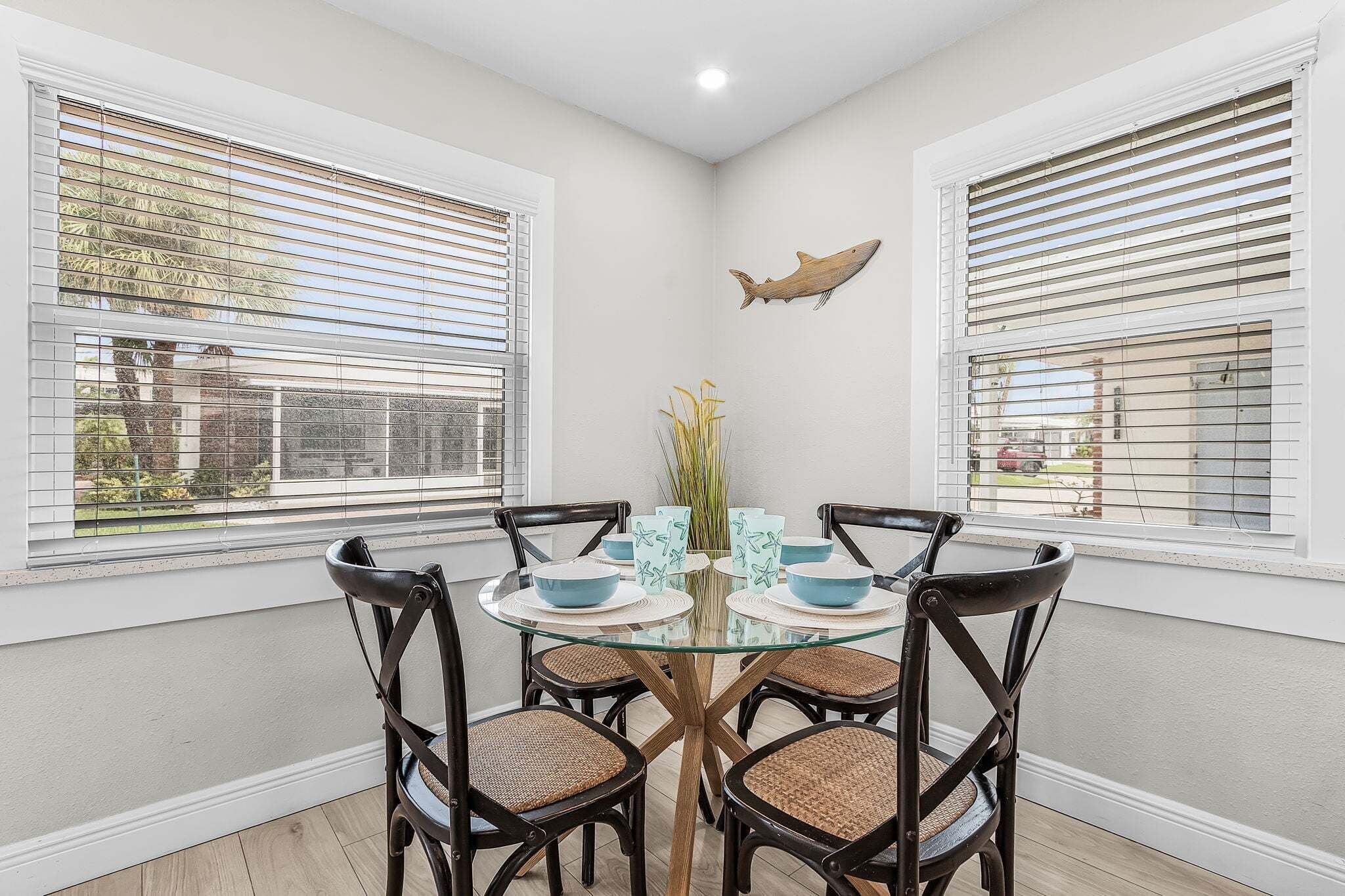 A dining area with a round glass table surrounded by four chairs, each with a woven seat.