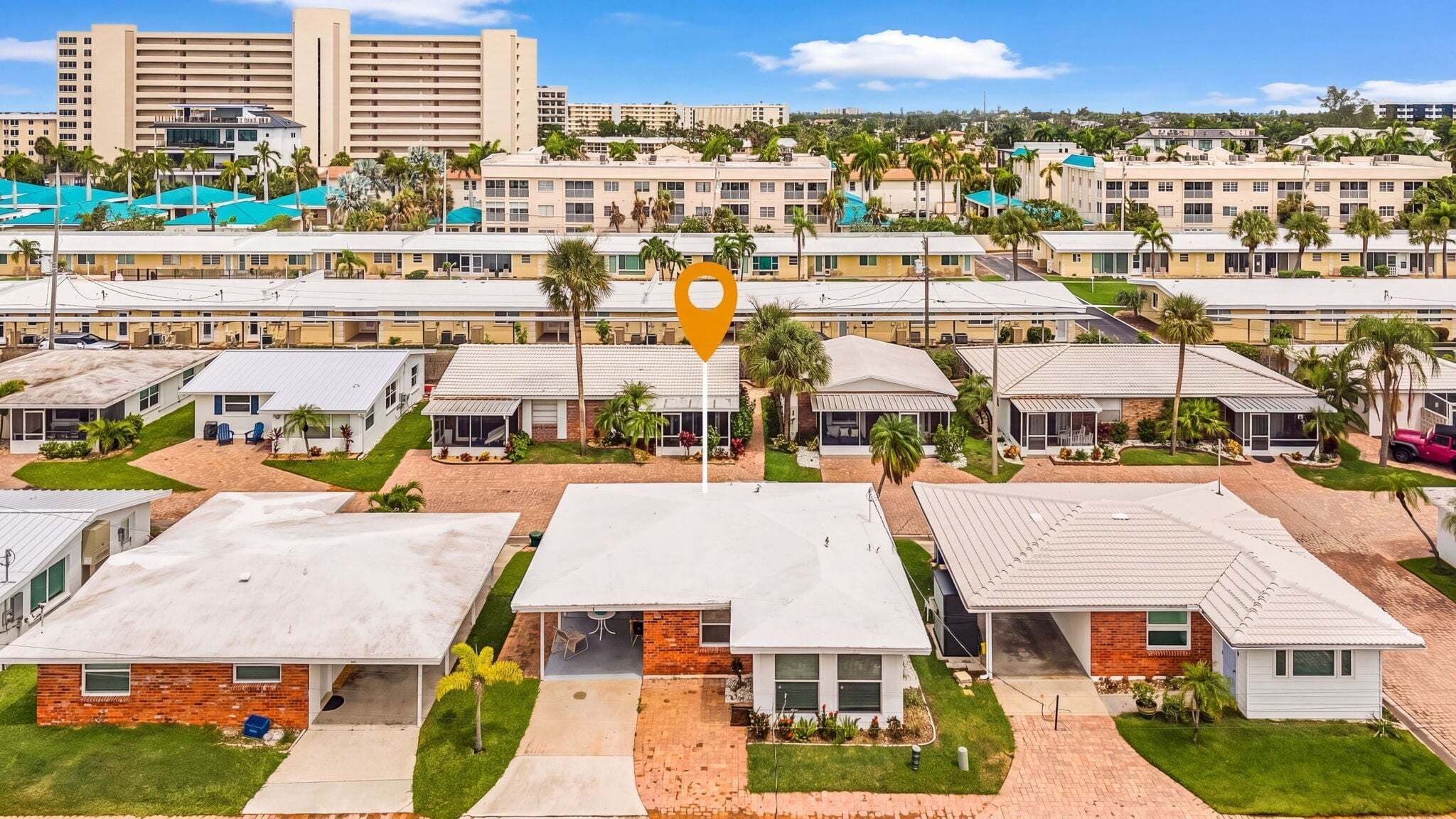 A cluster of single-story buildings with a central parking area, surrounded by palm trees and a clear sky.