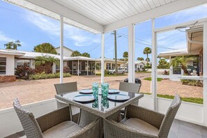 A covered outdoor patio with a table and chairs, a grill, and a view of neighboring houses.