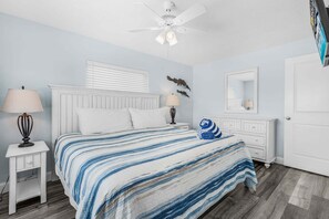 Quarto com uma cama, duas mesas de cabeceira, um ventilador de teto, um espelho e uma porta.