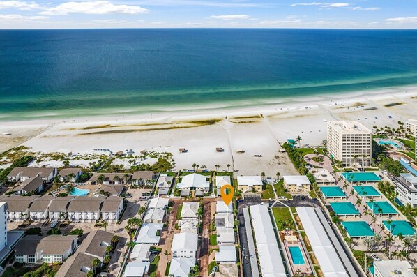 Vista aérea de un complejo turístico frente a la playa, con propiedades en primera línea, una piscina y un gran edificio hotel.