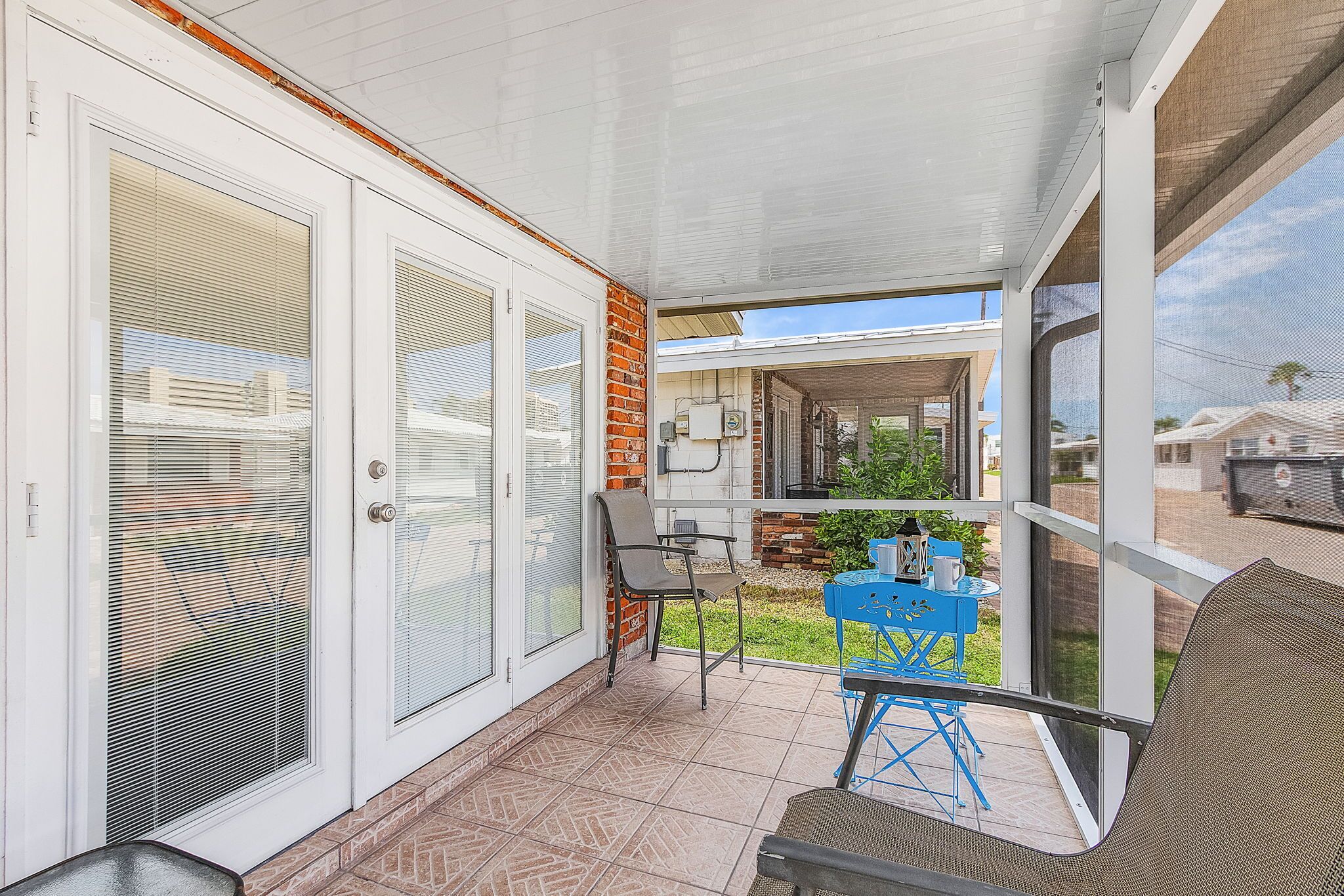 A covered patio area with a table and chairs, a sliding glass door, and a view of a neighboring house.