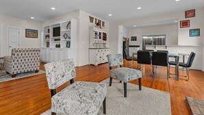 A spacious living room with a dining area, white cabinetry, and a kitchen in the background.