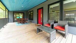 A covered outdoor area with a wooden deck, wicker furniture, and a red door.