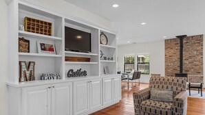 A spacious living room with a white entertainment unit, a comfortable armchair, and a wooden coffee table.