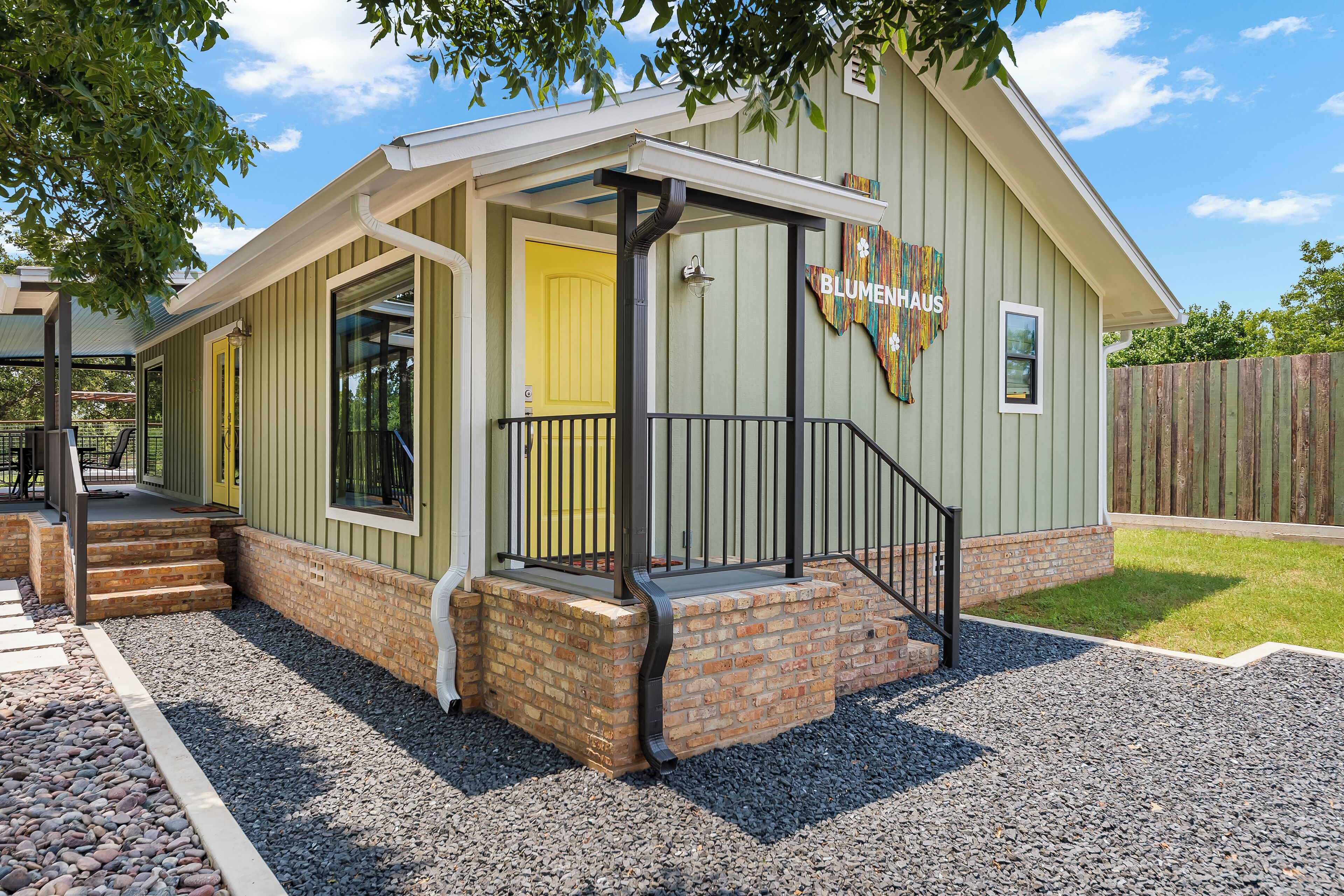 A green building with a yellow door, a brick base, and a sign reading "BLUMENHAUS".