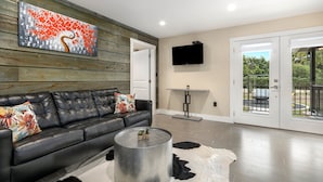 A modern living room with a black leather sofa, a round coffee table, and a large abstract painting on the wall. - Blumenhaus | Hot Tub | Fire Pit (Fredericksburg)