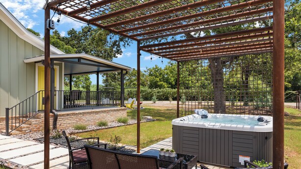 A covered patio area with a hot tub, outdoor seating, and a pergola. - Blumenhaus | Hot Tub | Fire Pit (Fredericksburg)