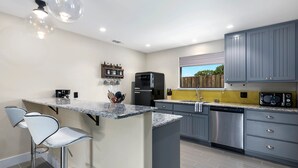 A modern kitchen with a central island, bar stools, stainless steel appliances, and a yellow backsplash. - Blumenhaus | Hot Tub | Fire Pit (Fredericksburg)