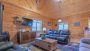 Un intérieur de chalet chaleureux, avec un revêtement mural en bois, des meubles en cuir, un téléviseur à écran plat et une cheminée.