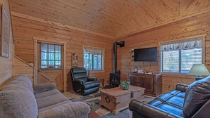 L’intérieur d’un chalet confortable, avec une cheminée, des canapés en cuir et un téléviseur.