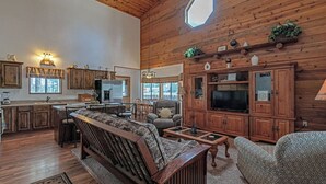 A spacious living area with a wooden ceiling, a large window, and a cozy seating arrangement. - Big Pines Ponderosa Cabin (Overgaard)