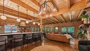 Un vaste espace de vie doté d’un plafond en bois, d’un bar avec des tabourets, d’un canapé et d’une cheminée.