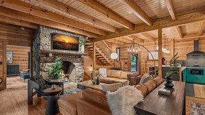 Un intérieur chaleureux de chalet en bois avec une cheminée en pierre, des poutres apparentes, un escalier et une cuisine moderne.