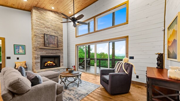 Un salón espacioso con chimenea, ventilador de techo y ventanas grandes con vistas al exterior.