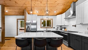 Una cocina moderna con una isla central, taburetes negros, electrodomésticos de acero inoxidable y techo de madera.