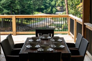 Une terrasse en bois avec une table dressée pour le repas, entourée de chaises, donnant sur un jardin aménagé.