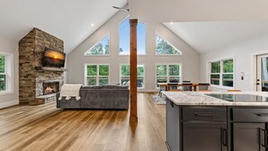 Ein geräumiger Wohnbereich mit Kamin aus Stein, einem grauen Sofa und einem Essbereich mit Holztisch und Stühlen.