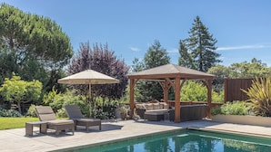 Ein Garten mit Schwimmbad, Liegestühlen, einem Holzpavillon und einer Pergola.