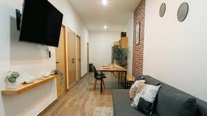 A modern living room with a dark grey sofa, wooden floor, a ceiling fan, a flat-screen TV mounted on the wall, and a dining area with a table and chairs. - Apartment next to the Malecon of La Paz BCS "DON MANOLO". (La Paz)