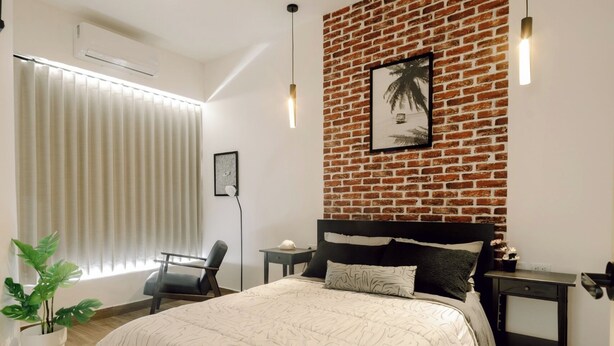 A modern bedroom with a brick-patterned wall, a large bed with a patterned bedspread, a desk, a chair, and a potted plant. - Apartment next to the Malecon of La Paz BCS "DON MANOLO". (La Paz)