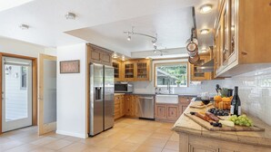 A modern kitchen with wooden cabinets, stainless steel appliances, and a central island with a fruit and cheese board. - New Listing! Water & Vine In Sebastopol (Sebastopol)