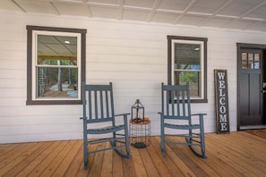 A porch with two rocking chairs, a small table with a lantern, and a 'WELCOME' sign.