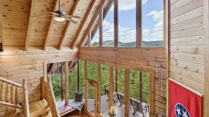 A wooden cabin with a loft bedroom, a balcony with a view of the mountains, and a flag on the railing. - The Cabin - 2 Bedroom with Breathtaking Mountain Views! Hot Tub, and Game Room (Sevierville)