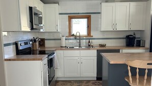 Une cuisine moderne avec des meubles blancs, un évier en acier inoxydable et un îlot central en bois doté d’un tabouret de bar.