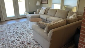 Un salon avec un canapé d’angle beige, une table basse ronde et un tapis à motifs.