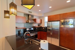 A modern kitchen with stainless steel appliances, wooden cabinets, and pendant lighting.