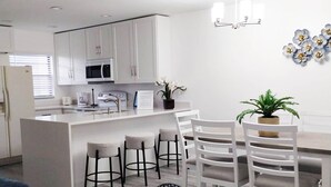 Une cuisine moderne avec des meubles blancs, un îlot central doté de tabourets de bar et un coin repas avec des chaises blanches.