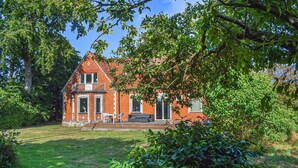 Een rode bakstenen woning met een balkon, gazon en omliggende groen.