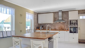 Een moderne keuken met witte kasten, een houten eiland met twee witte stoelen, een roestvrijstalen spoelbak en een inbouwoven.