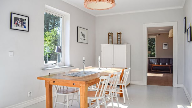 Een eethoek met een houten tafel en witte stoelen, een wit kastje en lijstwerken aan de wanden.