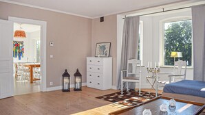 Een woonkamer met een houten salontafel, een witte bank, een eethoek met een houten tafel en stoelen, en een groot raam met gordijnen.