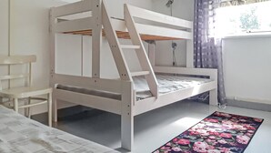 A bunk bed with a ladder, a chair, and a floral rug in a room with white walls and a window with curtains. - Amazing home in Holmsjö (Holmsjö)