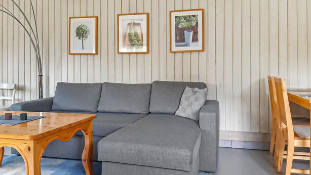 A modern living room with a grey sectional sofa, a wooden coffee table, and a dining area with a wooden chair. There are three framed pictures on the wall. - Amazing home in Holmsjö (Holmsjö)