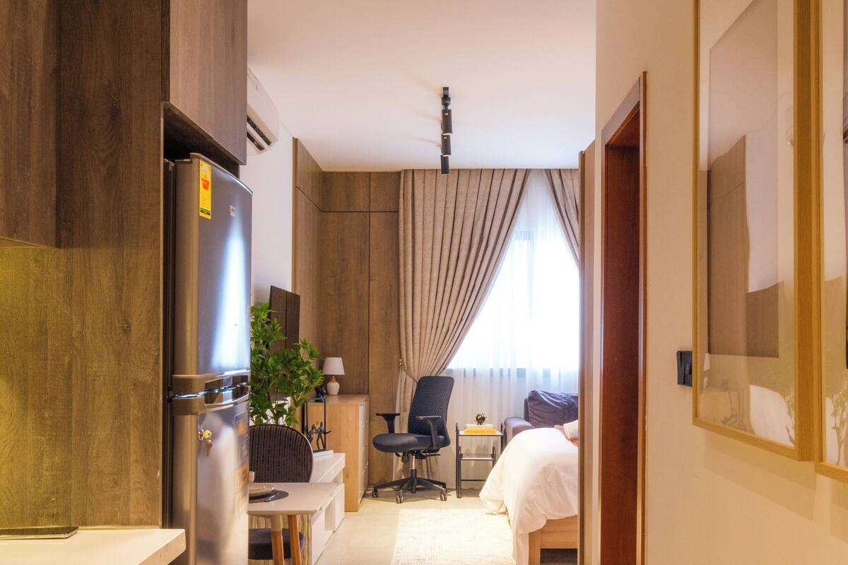 A hotel room with a kitchenette, a bed, a desk, and a chair.