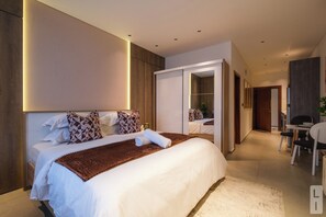 Une chambre d’hôtel moderne dotée d’un grand lit, d’un dressing, d’un coin repas et d’une salle de bain.