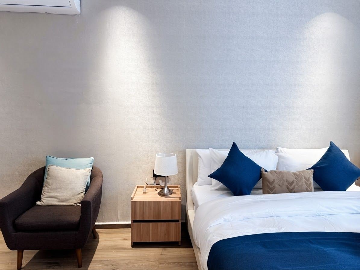 Una habitación de hotel con una cama, una silla, una mesita de noche y una lámpara.