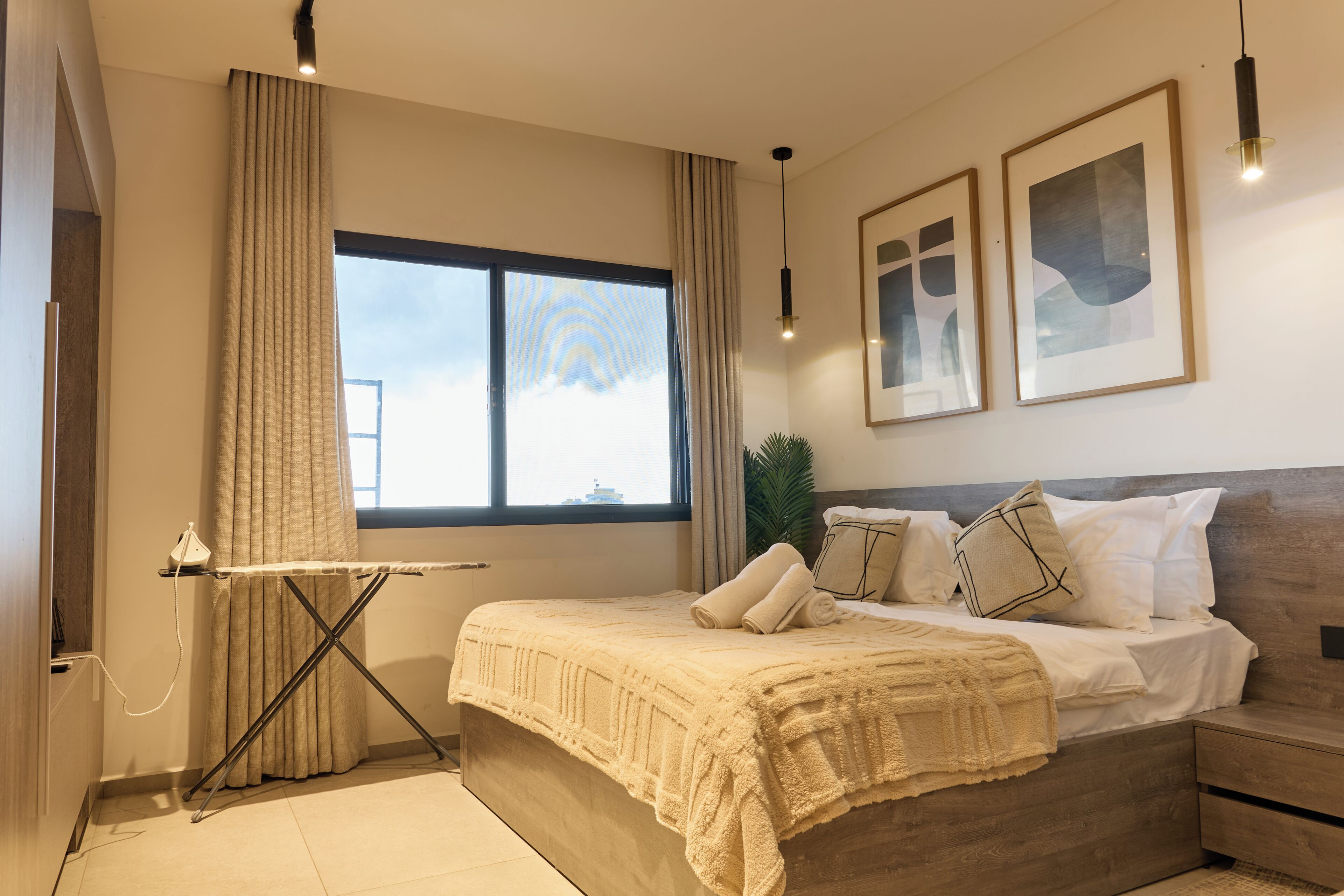Un dormitorio con cama, cortinas, una ventana y cuadros en la pared.