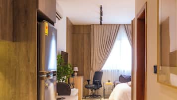 A hotel room with a kitchenette, a bed, a desk, and a chair.