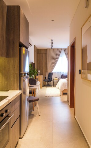 A hotel room with a kitchenette, a bed, a desk, and a chair. - Swiss Lodge, Labone (Accra)