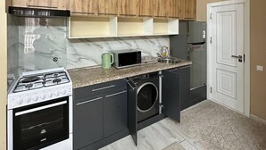 A compact kitchen with a gas stove, microwave, and built-in washing machine. - Apartments Tashkent cuty Gardens A1 (Tashkent)