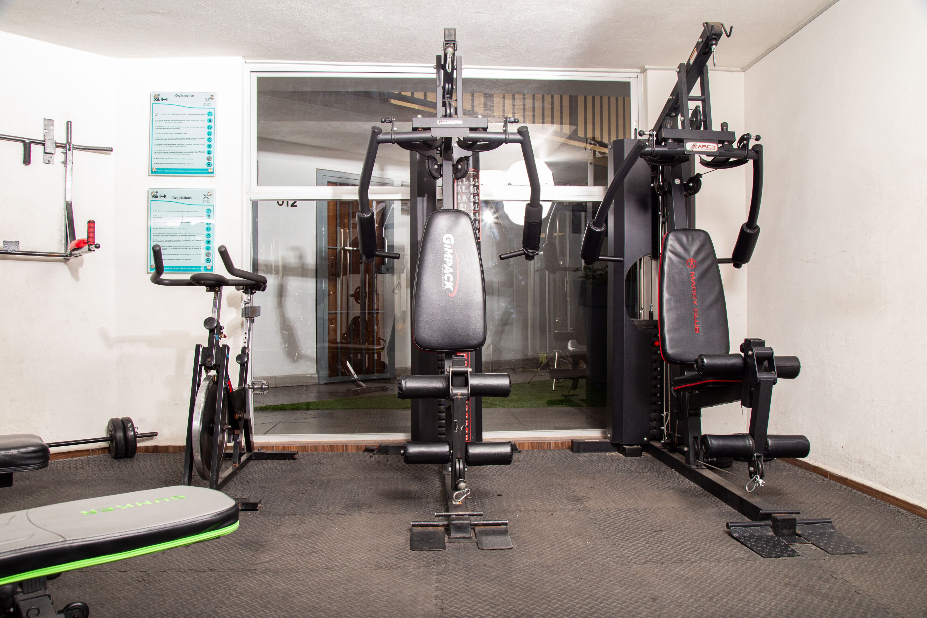 Een sportschool met trainingsapparatuur, een bank en een prikbord aan de muur.